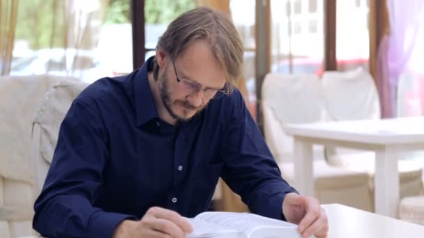 Caucasian man reading a book in the café. Portrait of a young man with a book in the restaurant. Stylish young man. Education, Lifestyle. — Stock video