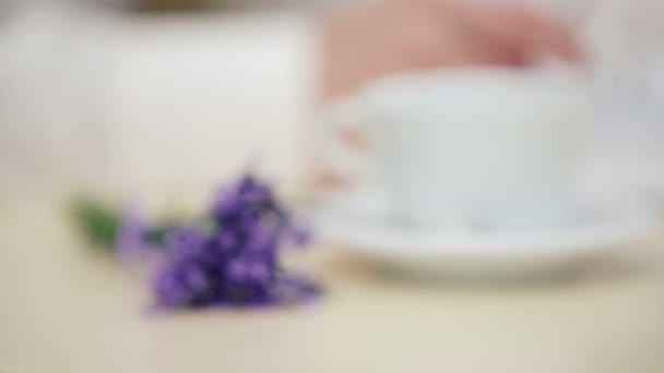 Mans hand with a close up of a cup and a bouquet of lavender. Hand of man with glasses on the background of the book. Hand, book, cup, flower, — Stock Video