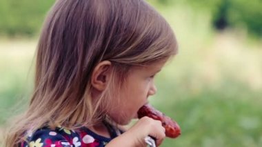 Beyaz küçük kız sosis mangal yiyor. Çocuk bir kız doğada yiyor. Emotsonalny çocuk sağlıklı gıda iştah açıcı yiyor. Bir yemek için bir çocuk portresi.