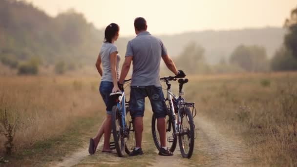 Ein junges Paar genießt das Radfahren in der Natur. Mann und Frau gehen, radeln. junges verliebtes Paar auf einem Feld. Sport, Freizeit, Lifestyle. — Stockvideo