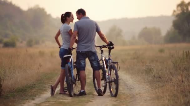 Młoda para się na rowerze w przyrodzie. Mężczyzna i kobieta, trasy spacerowe i rowerowe. Młody zakochany, para spaceru w polu. Rekreacja, sport, styl życia. — Wideo stockowe