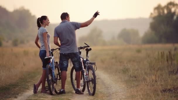 Um jovem casal que gosta de andar de bicicleta na natureza. Homem e mulher a andar de bicicleta. Jovem casal apaixonado andando em um campo. Desporto, recreação, estilo de vida . — Vídeo de Stock