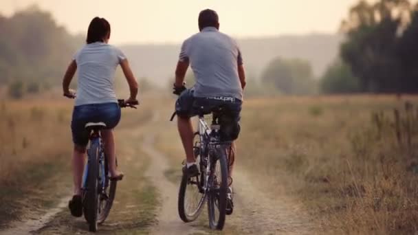 Młoda para się na rowerze w przyrodzie. Mężczyzna i kobieta, trasy spacerowe i rowerowe. Młody zakochany, para spaceru w polu. Rekreacja, sport, styl życia. — Wideo stockowe