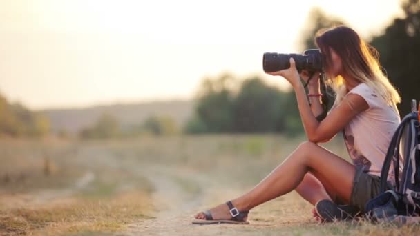 Hermosa joven periodista en la estepa. Chica con cámara en la naturaleza. Una joven con una cámara en un safari. Viajes, turismo, aventura . — Vídeo de stock