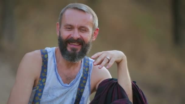 Retrato de un hombre hipster primer plano. Joven hombre barbudo emocional mirando a la cámara. La cara del hombre con barba en la naturaleza . — Vídeos de Stock