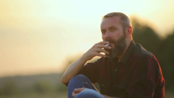 Retrato de un hombre barbudo con un cigarrillo. Emocional hombre fuma en la cámara . — Vídeo de stock