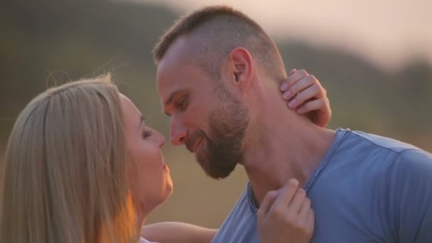 Um jovem e uma mulher no parque ao pôr-do-sol. Jovem casal feliz desfrutando de um momento íntimo sobre a natureza. Retrato de um jovem casal abraçando e beijando . — Vídeo de Stock