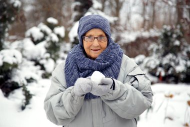 Kışın kartopu oynayan yaşlı bir kadının portresi. Yaşlı bir kadın kışın kartopu oynar..