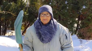 Kışın elinde kar küreği olan yaşlı bir kadının portresi. Yaşlı bir kadın kışın kürekle karı temizler..