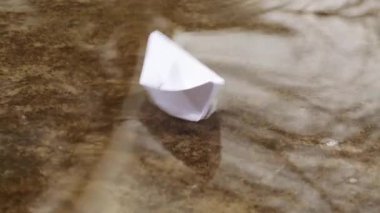 Baharda su birikintisinde kağıt tekne. Su birikintisindeki kağıttan bir teknenin yansıması..