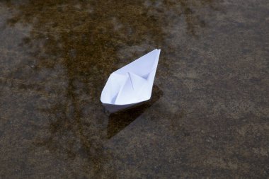 Baharda su birikintisinde kağıt tekne. Su birikintisindeki kağıttan bir teknenin yansıması..