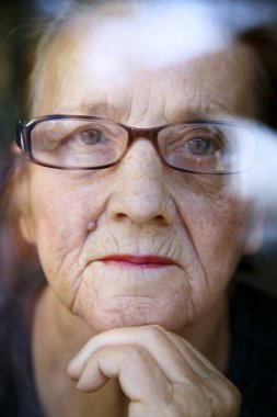 Pencereye yansıyan gözlüklü yaşlı bir kadının portresi. Pencereden dışarı bakan yaşlı bir kadının yüzü..