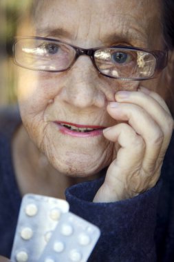 Pencerede elinde haplarla yaşlı bir kadının portresi. Gözlüklü yaşlı bir kadın pencerede ilaç tutuyor..