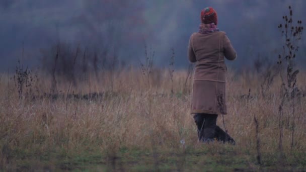 Ung kvinna med en hund på en promenad. Ung tjej med en hund i fältet. Ung kvinna i varma kläder i ett fält. — Stockvideo