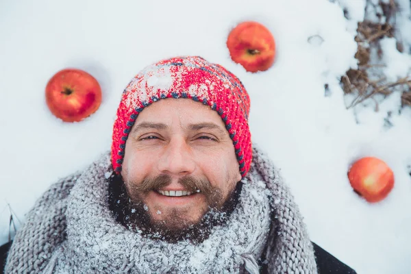 The face of a bearded man lying in the snow under the apple tree. Close up portrait of a bearded man near the apple tree in the winter.