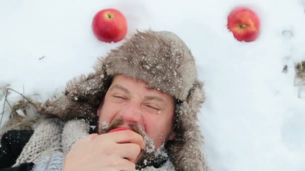 Porträtt av en skäggig man med ett äpple på vintern. En ung skäggig man äter ett äpple på vintern. Den skäggiga mannen äta ett äpple till kameran på vintern. — Stockvideo