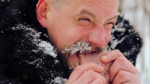 Retrato de un hombre con barba devorando carne cruda. El hambriento barbudo del norte come carne. Sobreviviente hombre barbudo del norte con un pedazo de carne . — Vídeos de Stock