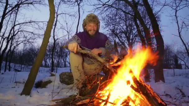 Bearded man warming his hands by the fire in winter. Tourist man evening campfire. A young bearded man at a fire in the woods. — Stock Video