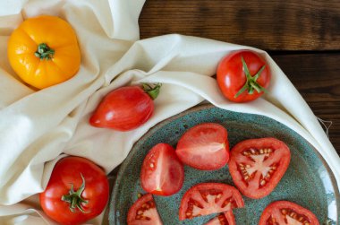 Dilimlenmiş domatesler tabakta ve domatesler ahşap arka planda çarşaflarda. Üst görünüm.