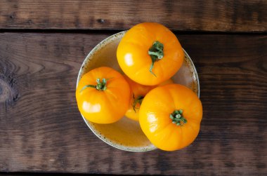 Yellow tomatoes in glazed clay bowl on wooden background. Top view.