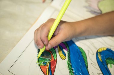 Bir çocuk beyaz bir masanın üzerine bir kalem çizer.