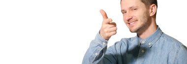 Genç, yakışıklı, soyutlanmış, mutlu, gülümseyen, işaret eden, parmaklarıyla başparmağını kaldıran bir adam.