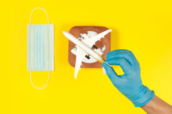 Plane model in hand, face mask  and earth model on a yellow background. Hands in gloves. Flight impact of coronavirus (COVID-19) concept. Afric