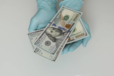 Mavi lateks eldivenli eller beyaz arka planda dolar banknotları tutuyor. Para, kazanç, kredi ve finans
