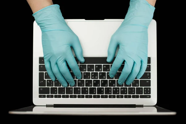 Hands in blue protective gloves typing on laptop keyboard. Top view. Coronavirus concept.