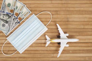 Uçak modeli, maske ve para fotokopi alanı olan ahşap bir arka planda. Uçuşların devamı. Coronavirüs kavramından sonra uluslararası uçuşların açılması (COVID-19)
