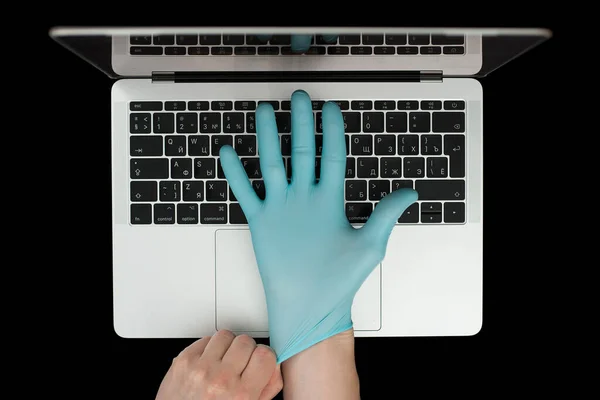 Hands in blue protective gloves typing on laptop keyboard. Top view. Coronavirus concept.