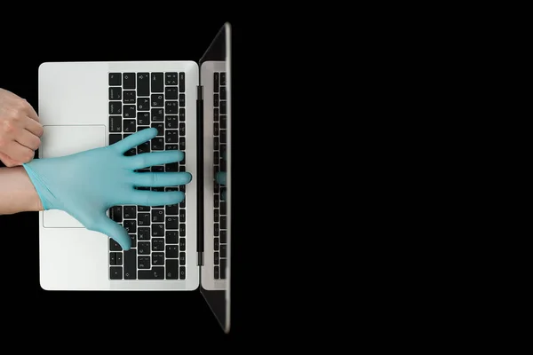 Hands in blue protective gloves typing on laptop keyboard. Top view. Coronavirus concept.