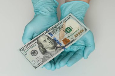 Mavi lateks eldivenli eller beyaz arka planda dolar banknotları tutuyor. Para, kazanç, kredi ve finans