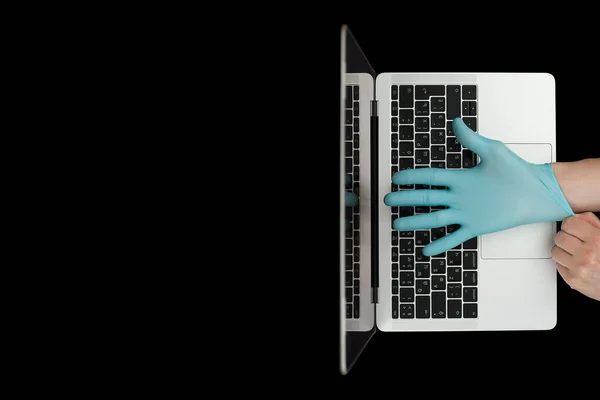 Hands in blue protective gloves typing on laptop keyboard. Top view. Coronavirus concept.