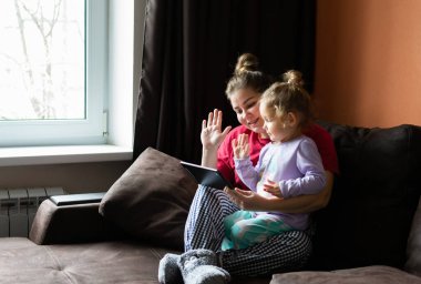 Anne ve kız sohbeti, evdeki tablet bilgisayarda video görüşmesi. Küçük kız elini ekranda sallıyor..