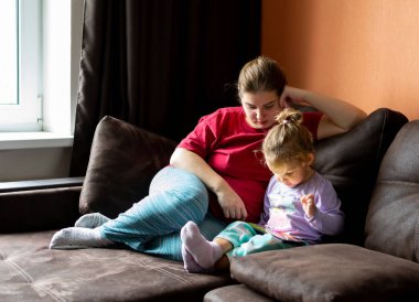 Anne ve kızı evde tablet kullanıyor. Annelik, bir çocukla vakit geçirmek. Ebeveyn sevgisi.