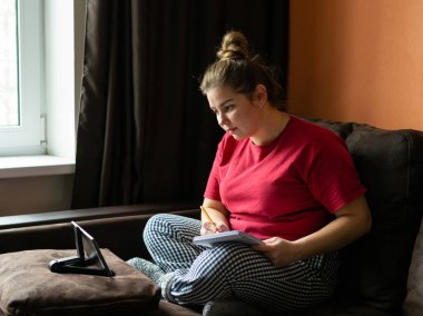 Genç bir kadın internet üzerinden tablet bilgisayardaki bir video konferans görüşmesiyle çalışıyor ve okuyor. Uzaklık eğitimi ve evden çalışma.