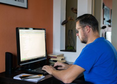 Gözlüklü, serbest çalışan bir adam, evdeki bir odada bilgisayar başında çalışıyor..