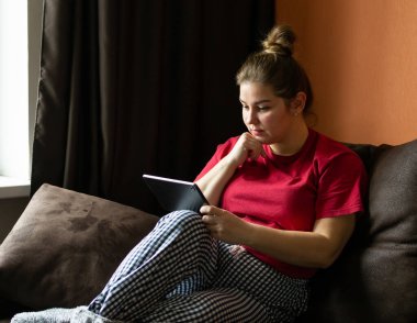 Çekici genç bir kadın evdeki kanepede otururken tablet bilgisayar kullanıyor..