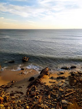 Sahil sükuneti. Okyanus dalgalarının, yumuşak, dağınık günbatımı ışığı altında kayalık ve kumlu bir plajla buluşmasının manzarası. Seyahat, dinginlik ya da kıyı temaları için mükemmel.