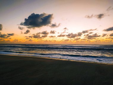 Okyanus üzerinde canlı bir gün doğumu yakalayan nefes kesici bir kıyı manzarası. Altın dalgalar ve dramatik bulutlar, seyahat, sağlık ve meditasyon temaları için mükemmel, barışçıl bir sahne yaratır..