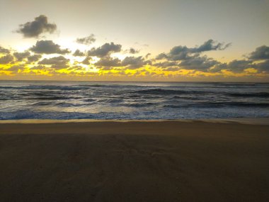 Yoğun bulutları, ritmik okyanus dalgalarını ve karanlık kumları aşan çarpıcı altın ışık. Bu sakin kıyı manzarası, seyahat, refah ve doğa temaları için mükemmel olan umudu çağrıştırıyor..