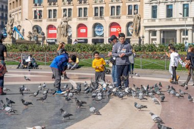 Barcelona, İspanya - 24 Şubat 2020: Yayalar güneşli bir kış öğleden sonra Plaza de Catalunya 'da güvercinleri besliyor