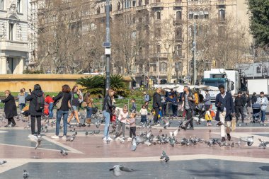 Barcelona, İspanya - 24 Şubat 2020: Yayalar güneşli bir kış öğleden sonra Plaza de Catalunya 'da güvercinleri besliyor