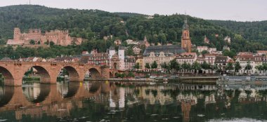 Heidelberg, Almanya - 1 Ağustos 2020: Yazın gün batımından sonra Neckar nehri kıyısındaki Heidelberg eski köprüsünün panoramik manzarası
