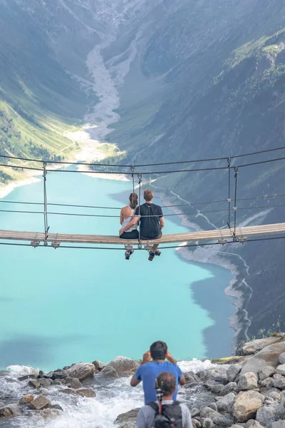 Olpererhutte, Rakousko - 7. srpna 2020: Muž fotí dvojici sedící na houpacím mostě na ledovcové nádrži — Stock fotografie