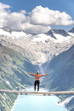 Half naked male sit on swing bridge viewing glacier in Zillertal Alps in summer clipart
