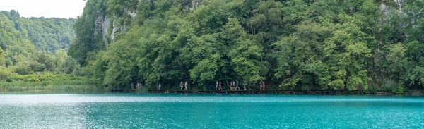 Plitvice, Croatie - 11 août 2020 : Vue panoramique des touristes marchant au bord d'un lac de couleur qaua — Photo