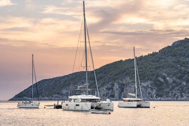 Komiza, Hırvatistan - 17 Ağustos 2020: Günbatımında adanın Adriyatik Denizi 'nde tekne ve yatlar katamaranları