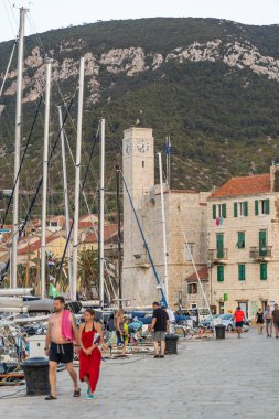 Komiza, Hırvatistan - 17 Ağustos 2020: Turistlerle birlikte adanın yaz mevsiminde balıkçı kalesi saat kulesinin liman manzarası